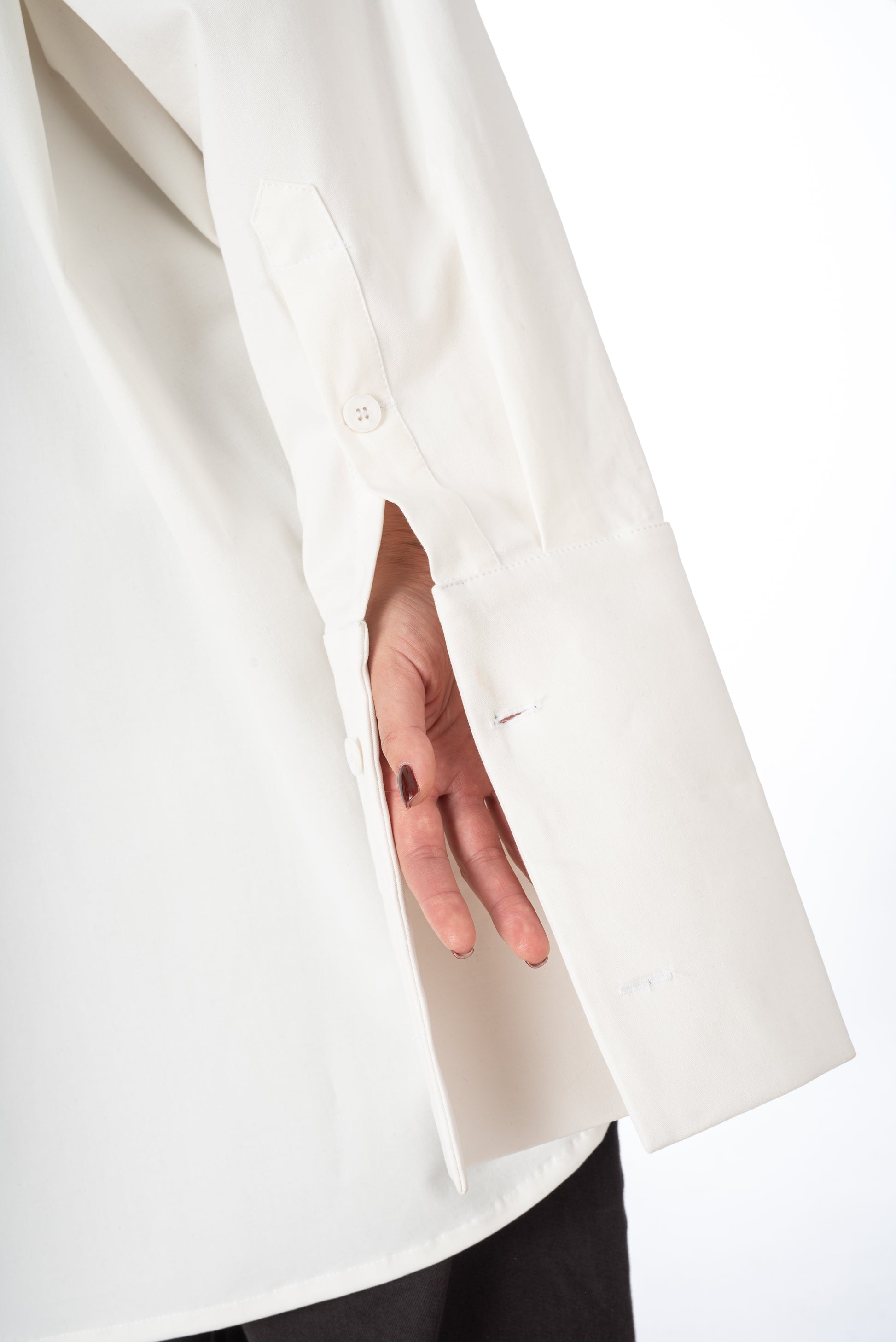 Close-up lifestyle image of an unfolded sleeve cuff on a white oversized shirt, emphasizing the button closure and stylish design.